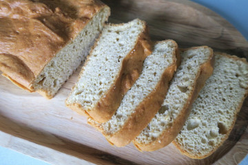 Close-up of a golden-brown, part-sliced loaf of keto nut-free bread on a wooden serving board.