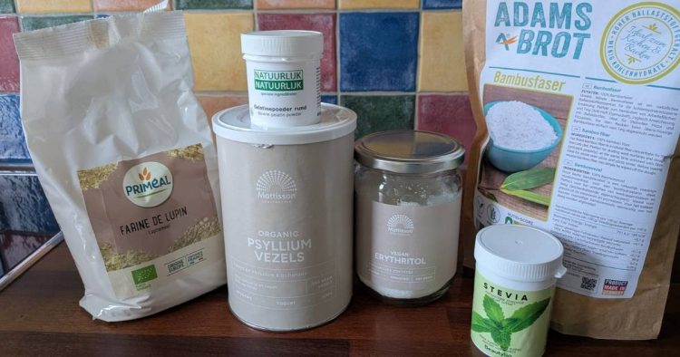 A bunch of keto ingredients on the kitchen counter. From left to right: lupin flour, gelatine powder, psyllium husk, erythritol, stevia, and bamboo fiber.